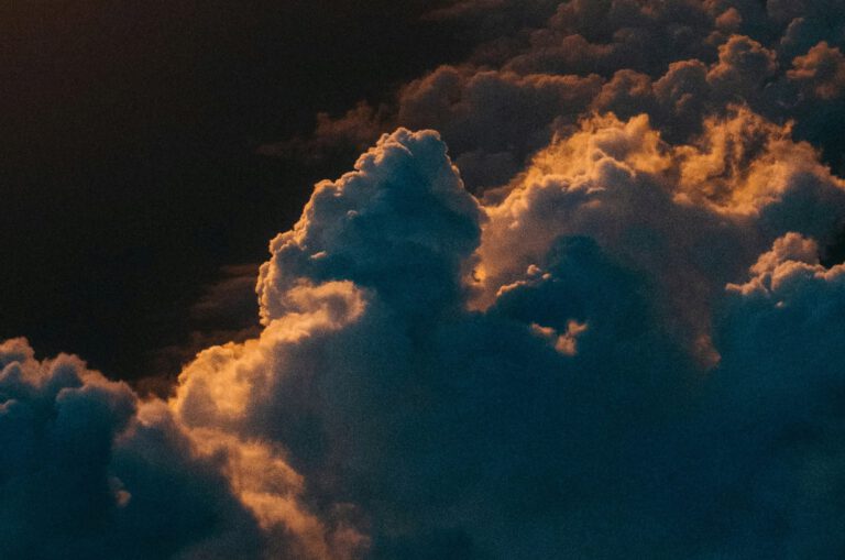 Aerial photograph of clouds, warmly lit in orange by a sunrise or sunset.
